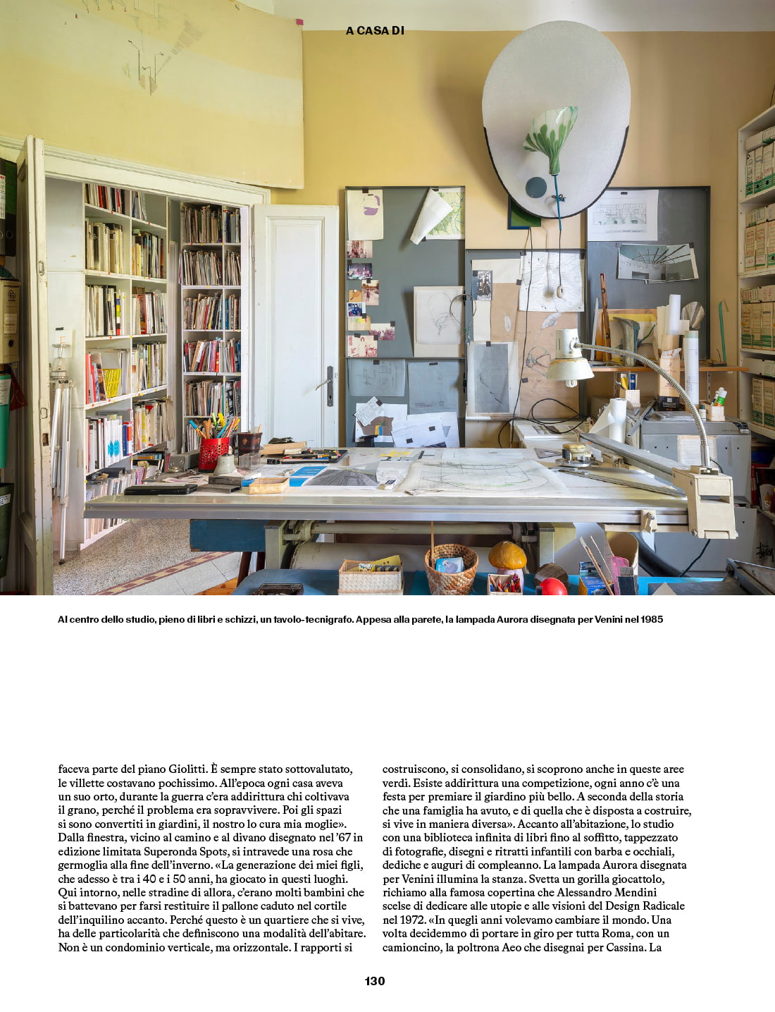 Paolo Deganello’s studio with a drafting table covered with drawings and bookshelves filled with books; the Aurora lamp designed for Venini hangs on the wall.
